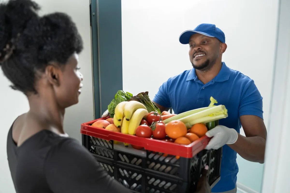 Coursier livrant un cageot de fruits et légumes à une cliente